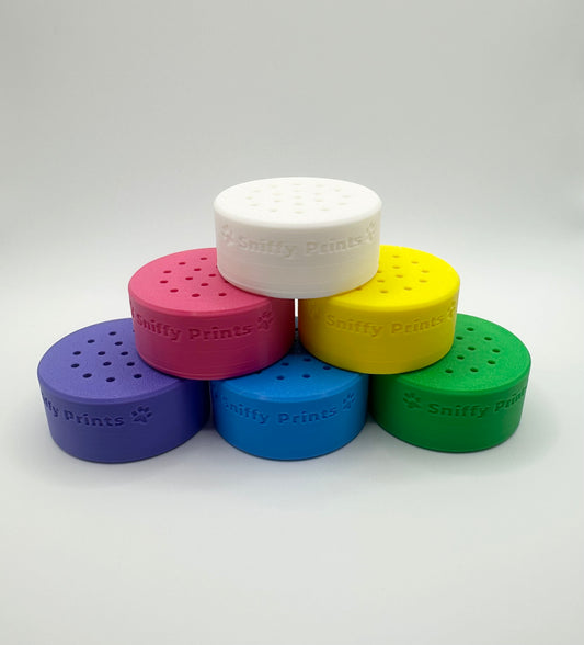 A set of colorful 3D-printed Odor Pods for K9 nosework, stacked in a pyramid formation. The pods are available in multiple colors, including pink, white, yellow, green, blue, and purple. Each pod has ventilation holes to allow odor dispersal during training.