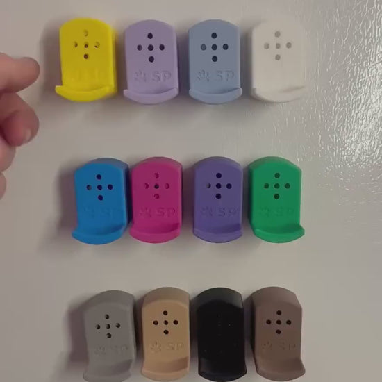A short video demonstrating how the Sniffy Prints pairing extensions for K9 nosework go over top of the Tiny Hides. The extensions in the video are magnetic and designed to go over Sniffy Prints Tiny Hides. They come in 12 different colors. Each piece features a curved base to hold a treat, multiple small holes for odor to pass through, and an embossed 'SP' logo with a paw print.