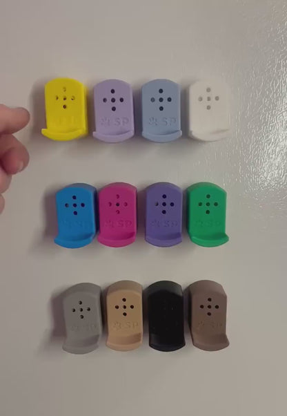 A short video demonstrating how the Sniffy Prints pairing extensions for K9 nosework go over top of the Tiny Hides. The extensions in the video are magnetic and designed to go over Sniffy Prints Tiny Hides. They come in 12 different colors. Each piece features a curved base to hold a treat, multiple small holes for odor to pass through, and an embossed 'SP' logo with a paw print.